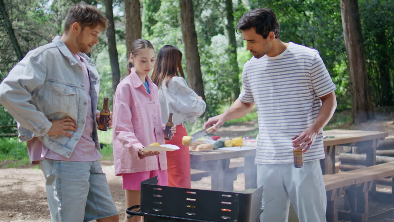Friends talking summer picnic in green forest. Group vacationers grilling food
