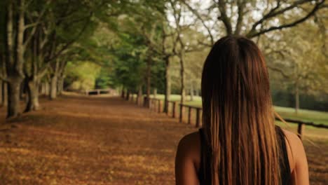 Middle-aged-Caucasian-girl-hiking-autumn-forest-trail-alone,-medium-close-up-backshot