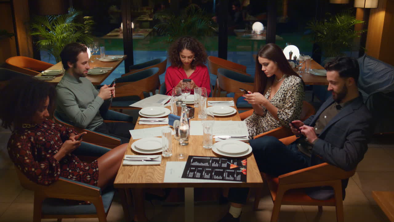 Multiracial group checking phone device in cafe. Friends texting in restaurant.