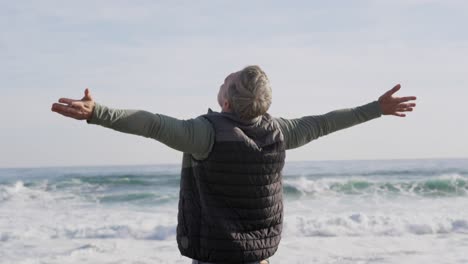 Caucasian-woman-enjoying-free-time-by-sea-on-sunny-day-standing-with-arms-wide