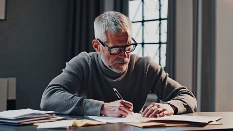 focused mature accountant in eyeglasses working with documents, sitting at desk, writing with pen on paper, analyzing financial reports, preparing audit or tax return
