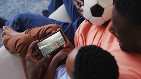 composite of father and son at home watching rugby match on smartphone