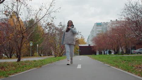 freelancer walking on tarred road adjusting hair while others walk by in hoodies and car parked in background with autumn trees, residential buildings, and green grass lining