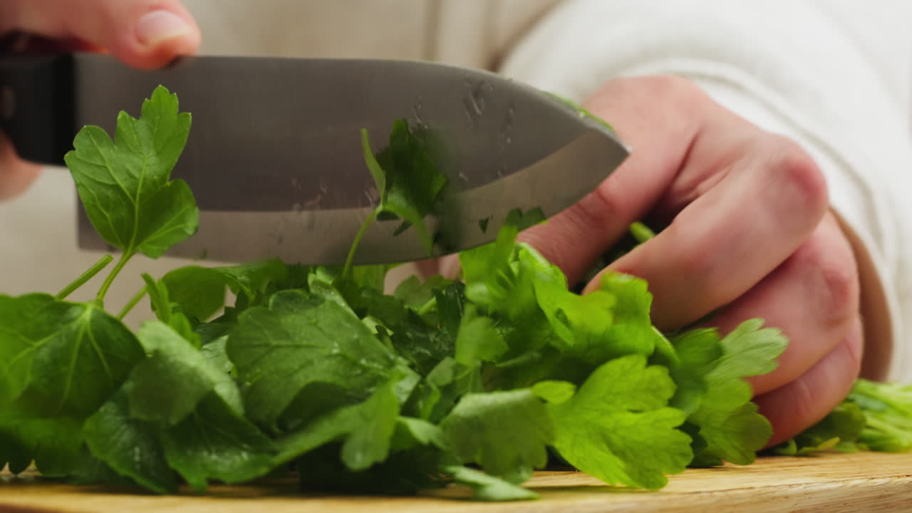 Close-up of Hands Chopping Fresh Parsley on a Wooden Cutting Board
