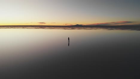 Aerial-of-a-lone-figure-slowly-walking-along-the-mirrored-reflection-of-the-world's-largest-salt-flat-at-dusk-in-Uyuni-Salt-Flats-,-Bolivia