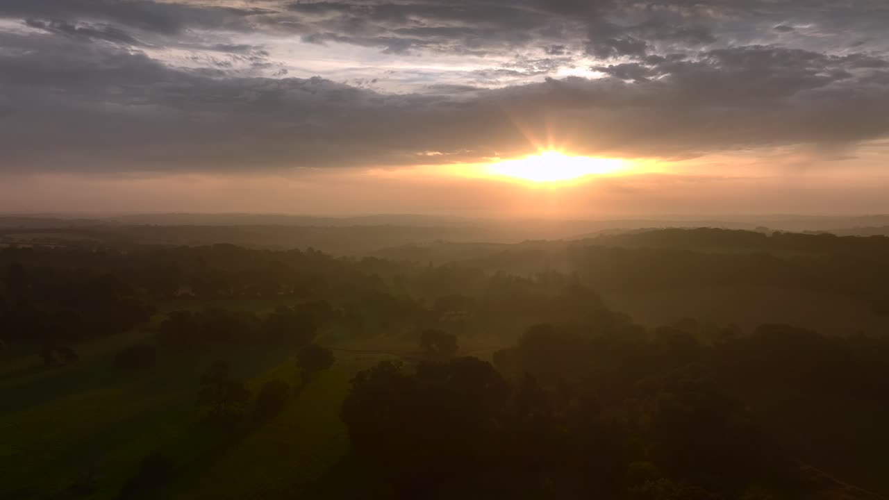 Misted woodland, fields and hedgerows at sunrise over lush rural South West English countryside. Summer. Cornwall, UK.