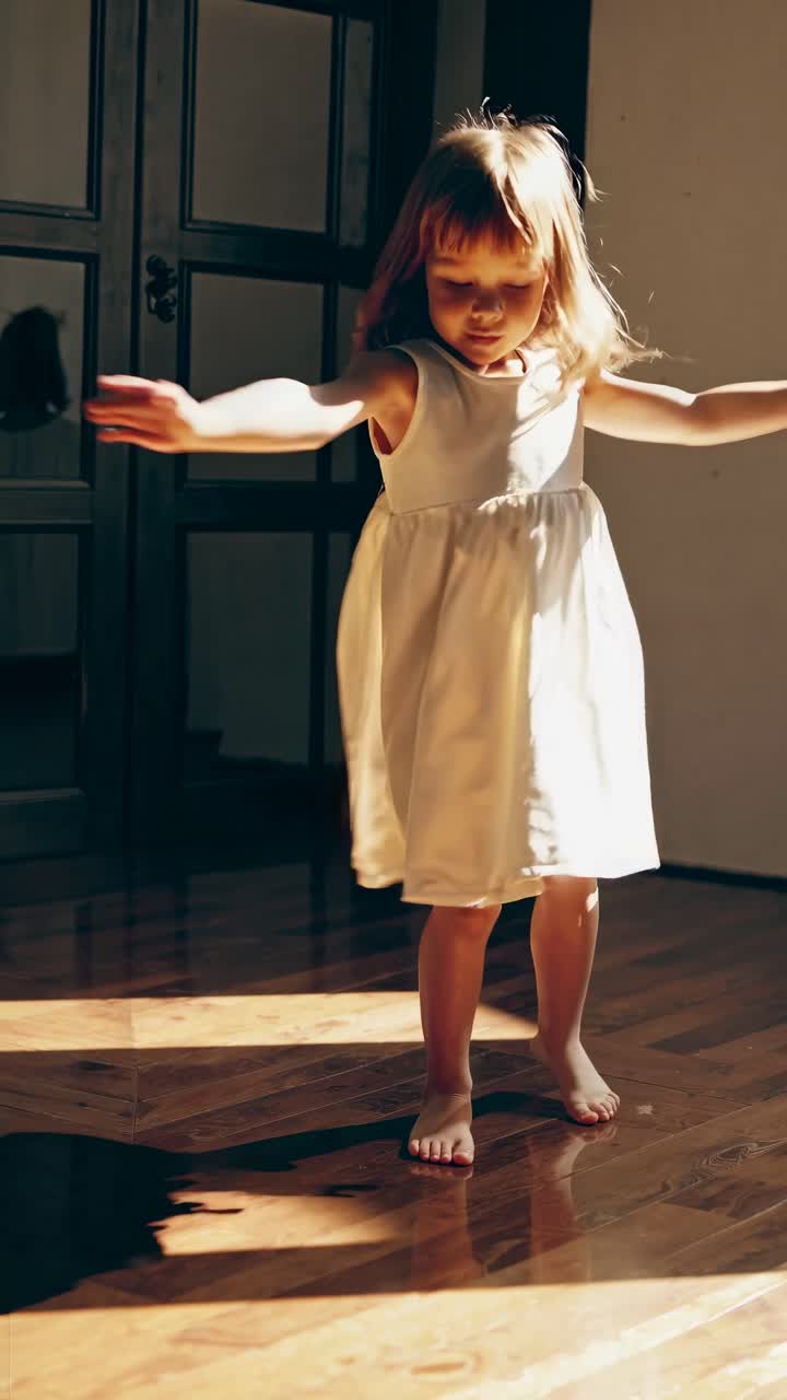 A child in a white dress dances in sunlight on a wooden floor