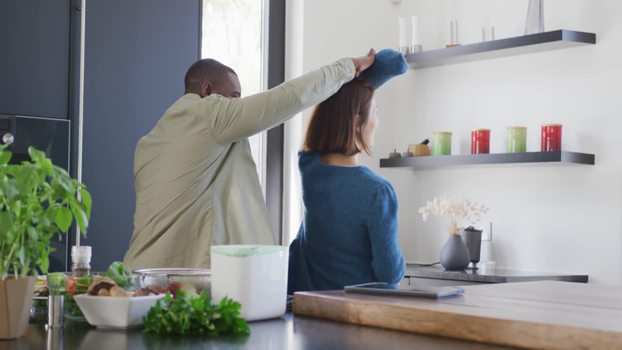 video de una feliz pareja diversa divirtiéndose bailando juntos en la cocina en casa