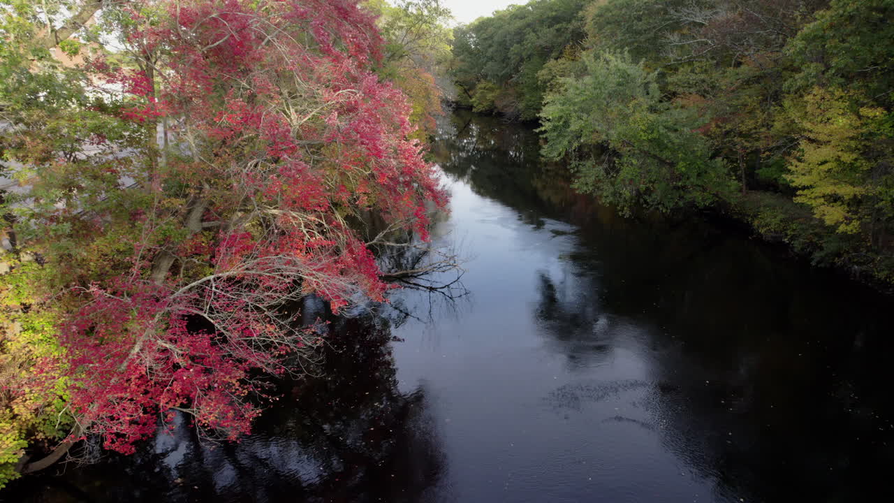 Aerial drone video of the peaceful Pawtuxet River in Cranston, Rhode Island lined with color changing fall foliage and bookended by a railroad bridge and a road bridge