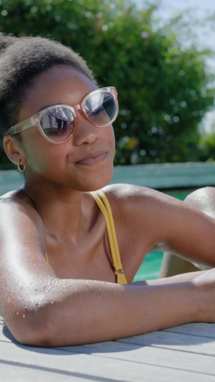 Vertical video: Smiling thirsty woman in yellow top lifting glass, sipping, leaning to man at pool