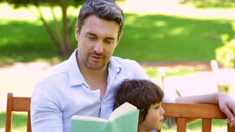padre e hijo sentados en un banco del parque leyendo