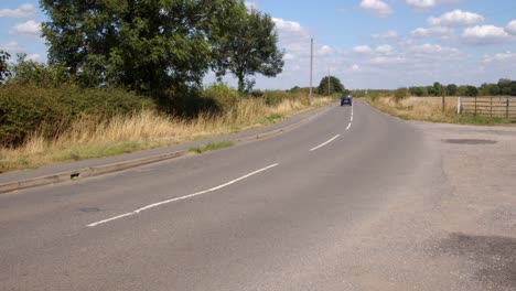 blue car driving away on a uk b road in the countryside