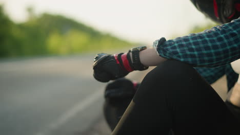 a close-up view of a female biker sitting alone on the side of a rural road, her gloved hand hitting her leg in a moment of contemplation