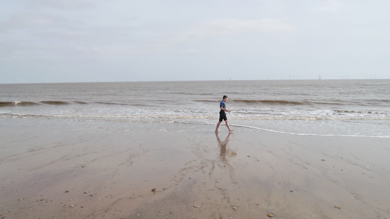 Young boy in a wetsuit on a beach digging in the sand. Playing with a surfboard and practicing skimming on the water. Seaside scene. Ocean waves breaking on the beach. Holiday time season