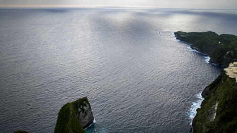 Nusa-Penida-cliffs-as-ocean-waves-crash-on-rocks-at-sunset,-aerial-time-lapse