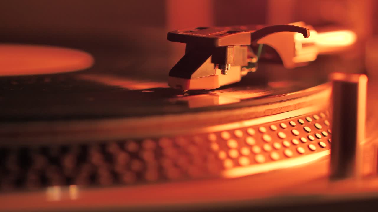 A Rotating Vinyl Record on a Turntable in the Light of a Warm Orange-Red Lamp. A dusty green colour LP Vinyl Disc Record Close-up Playing Music. Type F.