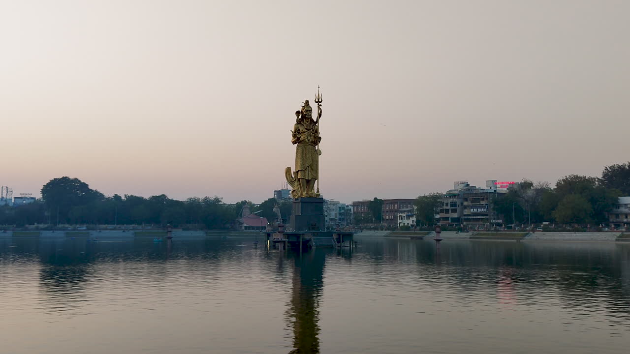 disfruta de una impresionante vista frontal de la inmensa estatua dorada del señor shiva en el lago sursagar en vadodara al anochecer