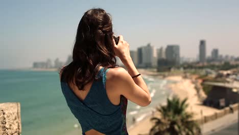 A-young-and-pretty-photographer-taking-a-photo-with-her-DSLR-camera-overlooking-a-beautiful-sandy-beach-on-a-hot-summers-day-in-america