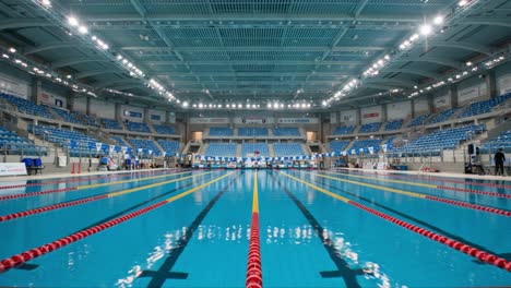 an impressive indoor swimming pool venue showcasing an expansive aquatic arena equipped with modern lighting and seating for spectators