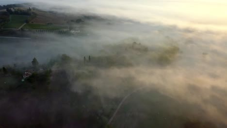 tuscany hills covered in morning mist clouds at sunrise, aerial drone view