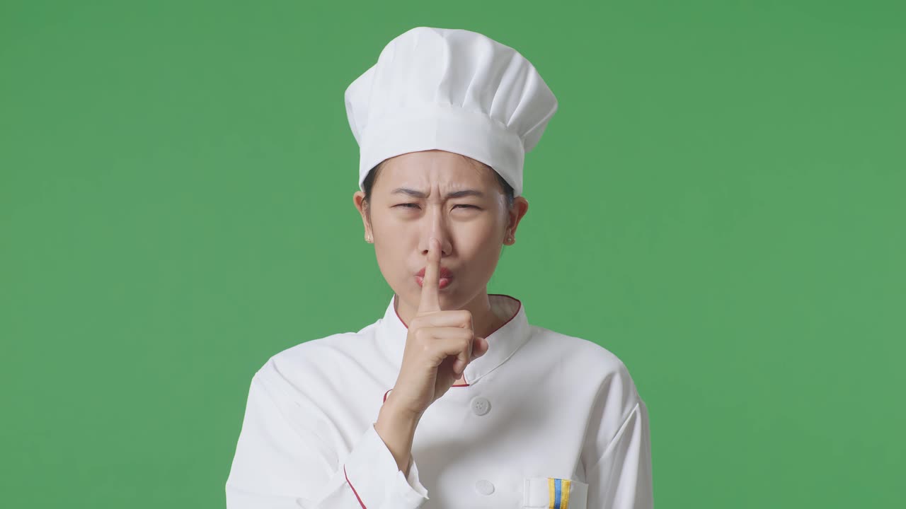 Close Up Of Asian Woman Chef Looking At Camera And Making Shh Gesture In The Green Screen Background Studio