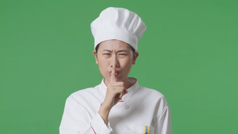 close up of asian woman chef looking at camera and making shh gesture in the green screen background studio
