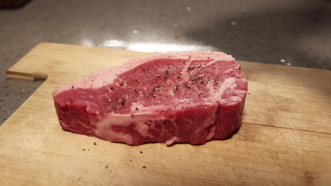 Seasoning a fresh beef steak with salt. Pouring salt on meat