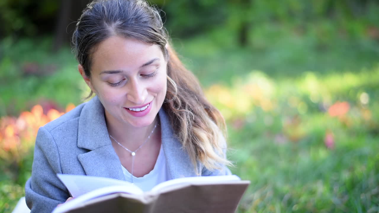 Donna bionda che legge un libro, sdraiata sull'erba in un parco