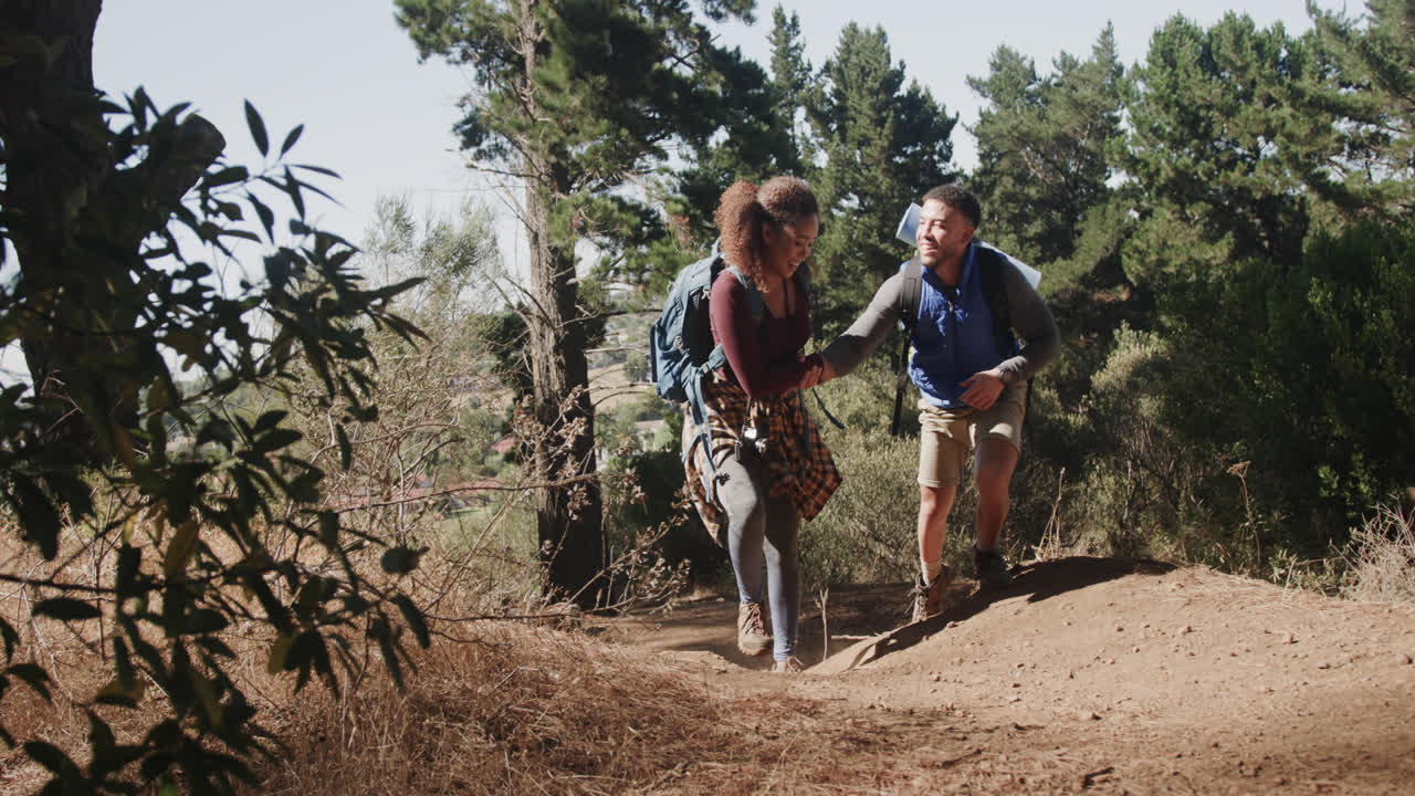 una feliz pareja afroamericana haciendo senderismo y usando mochilas en el bosque, en cámara lenta