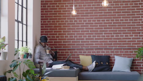 joven estudiante afroamericano hombre estudiando preparándose para un examen universitario navegando en línea investigación en computadora portátil bebiendo café ejoying escuchando música en la oficina