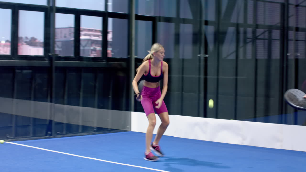 Woman playing padel tennis indoors, swinging racket with focus and determination, at indoor court