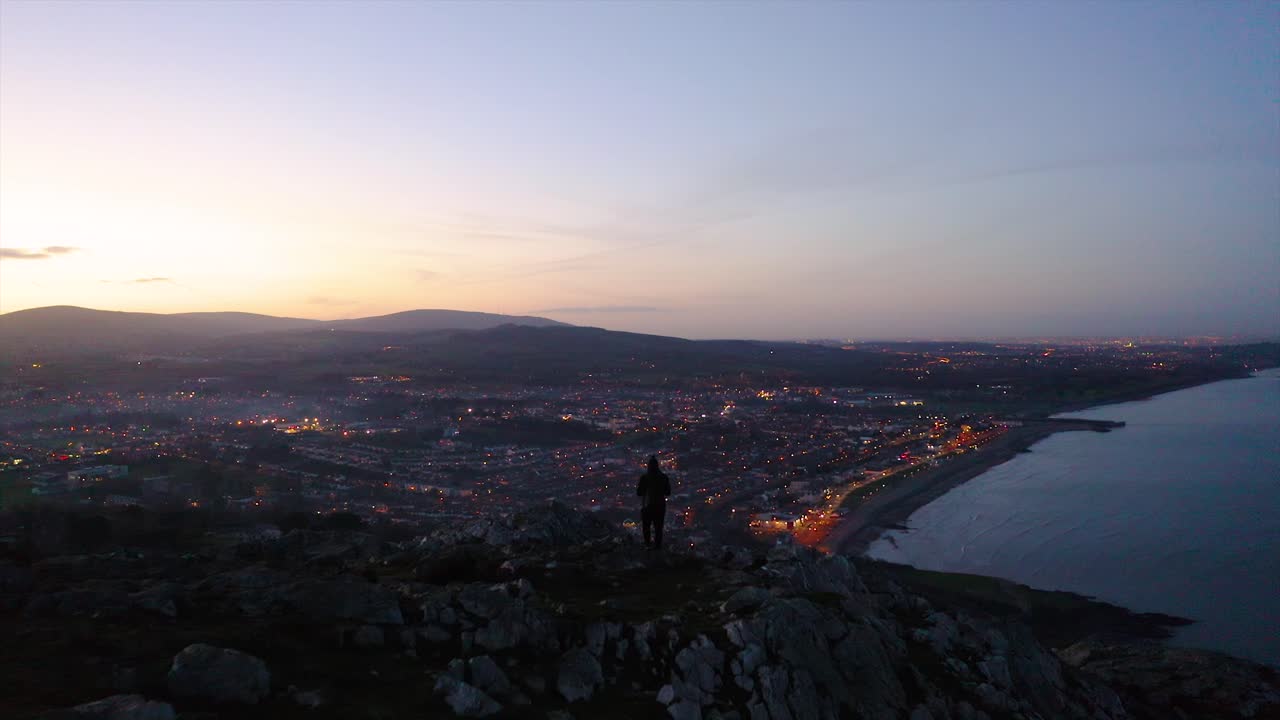 A clear sunset over Bray, Ireland. A person is walking towards the city lights while on the Bray mountain. The sea was very calm and absolutely no wind that day.