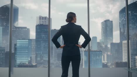 successful businesswoman in stylish suit looking out of the window at big city in downtown area. confident female ceo working on financial projects. real estate agent planning a development deal.