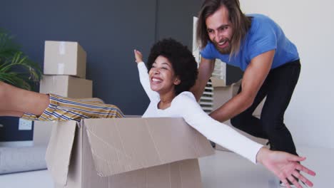 Caucasian man pushing his wife sitting in cardboard boxes at new apartment house
