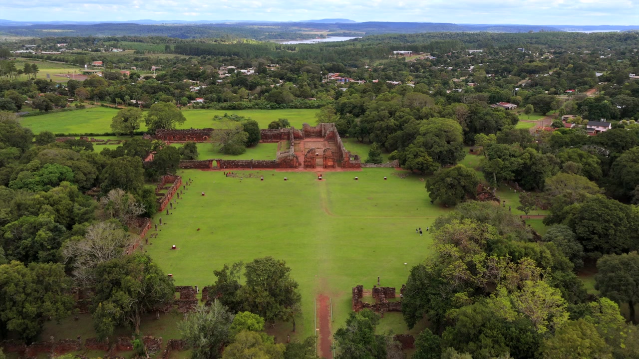 Le rovine di San Ignacio Mini sono immerse in un vibrante paesaggio verde, visibili accanto alla città. Utile per documentari storici e servizi di viaggio.