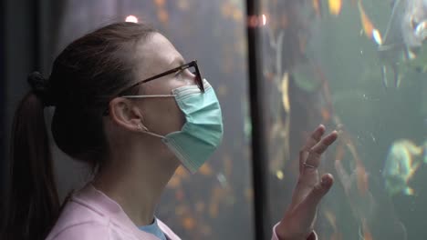 primer plano de una mujer con una máscara y tocando el cristal en el acuario mientras los peces nadan junto a ella