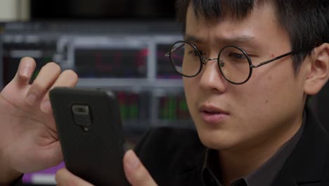 asian man stressed to see mobile with stock market in background