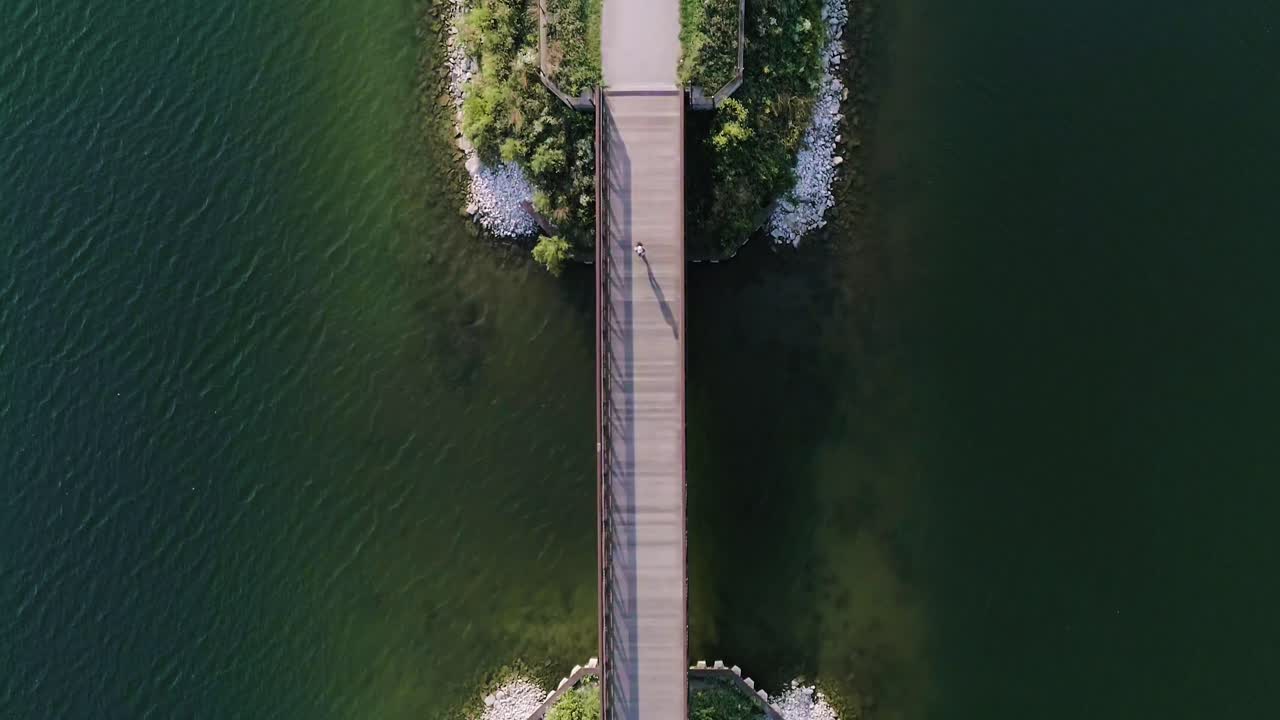 호수를 가로지르는 작은 다리를 가로질러 달리는 여성의 균형 잡힌 공중 샷