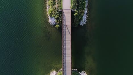 a balanced aerial shot of woman running across a small bridge spanning a lake