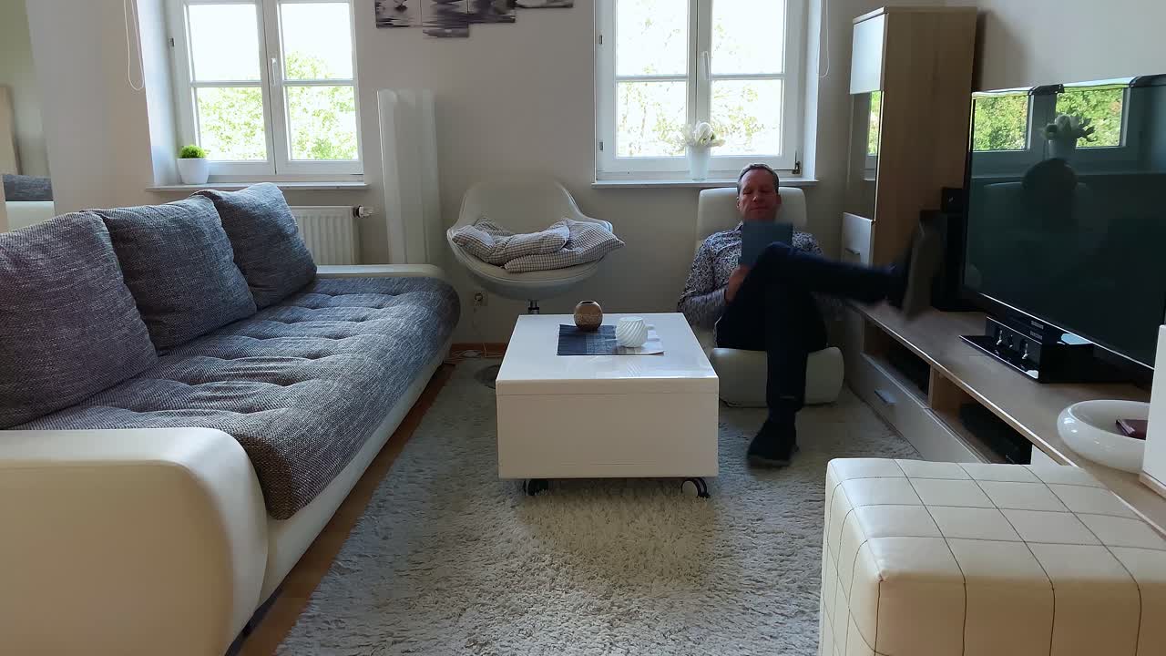 un hombre se sienta en una tumbona en la sala de estar y comienza a leer desde una tableta