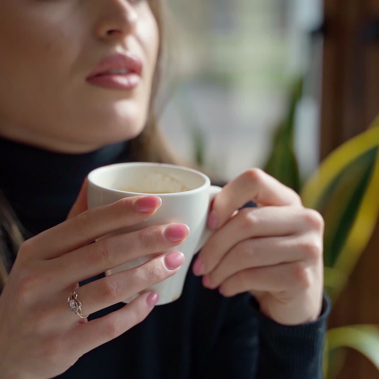 White cup with coffee in woman's hands. Beautiful young woman enjoying hot drink in a cafe. Slow motion.