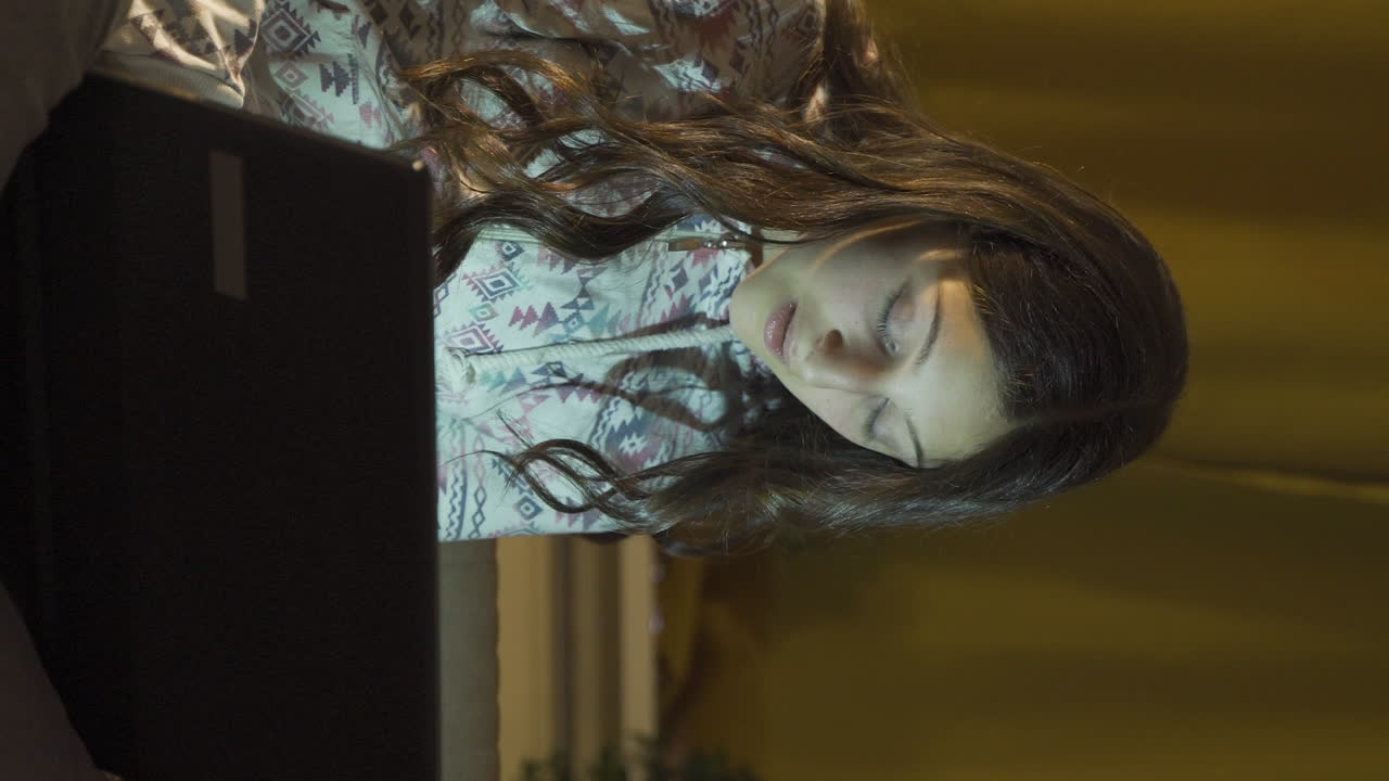 вертикальное видео молодой женщины, глядящей на ноутбук с удивлением ночью дома.