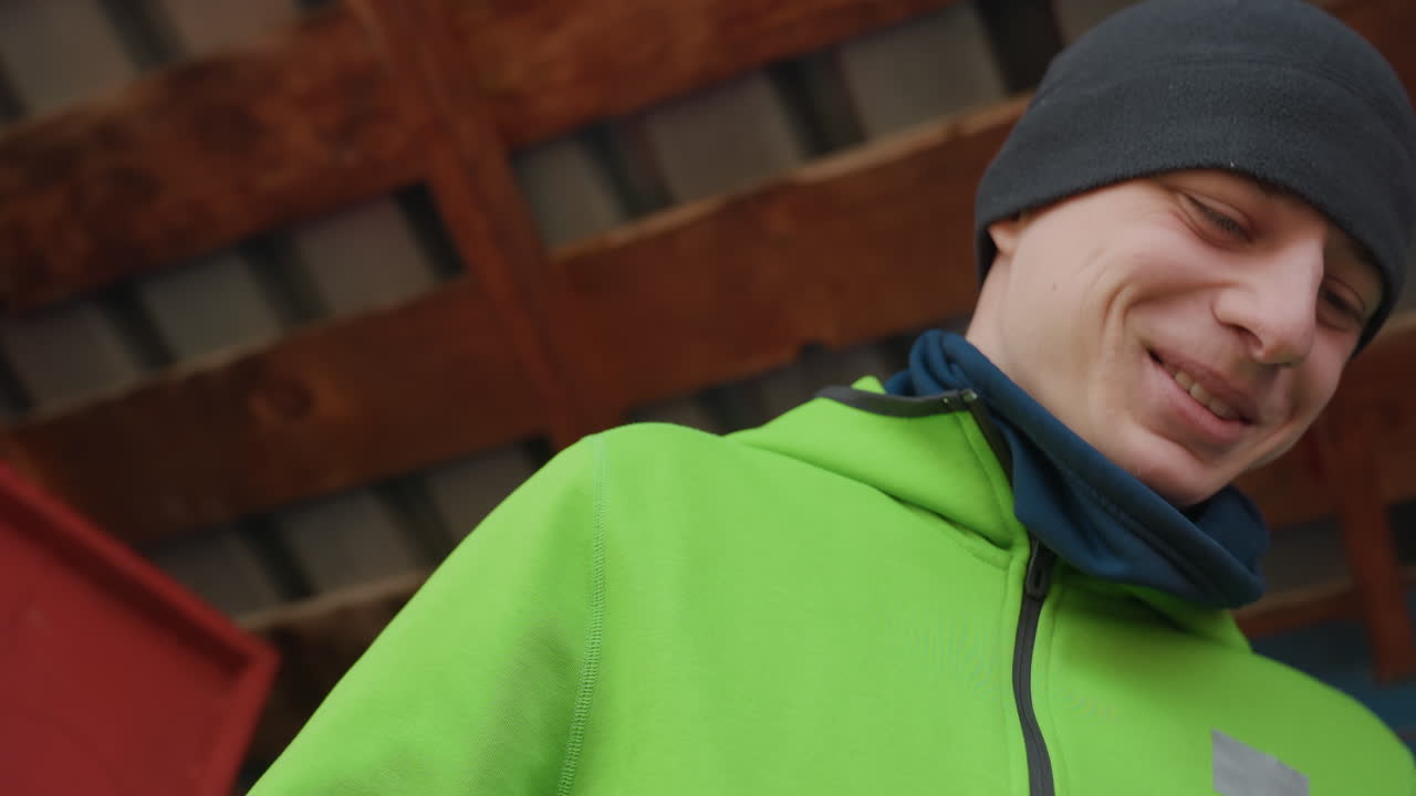 야외에서 활짝 웃는 남자, 미소 짓는 남자의 편안한 인물 사진, 캐주얼한 옷차림과 비니를 착용한 활기찬 남자가 등장하는 도시 풍경, 초록색 재킷을 입고 도시 풍경을 배경으로 야외에서 활짝 웃는 남자의 생동감 넘치는 인물 사진