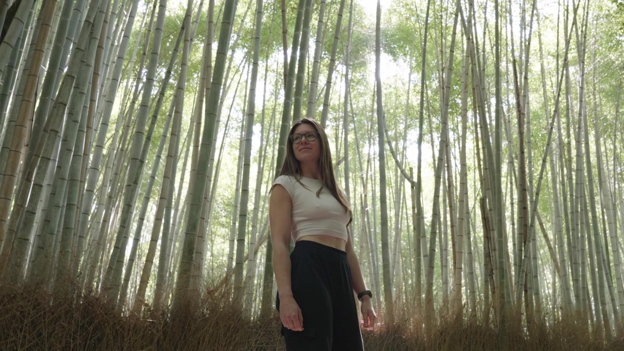 Young caucasian woman looking around in a bamboo forest in morning light at Arashiyama, Kyoto, Japan.