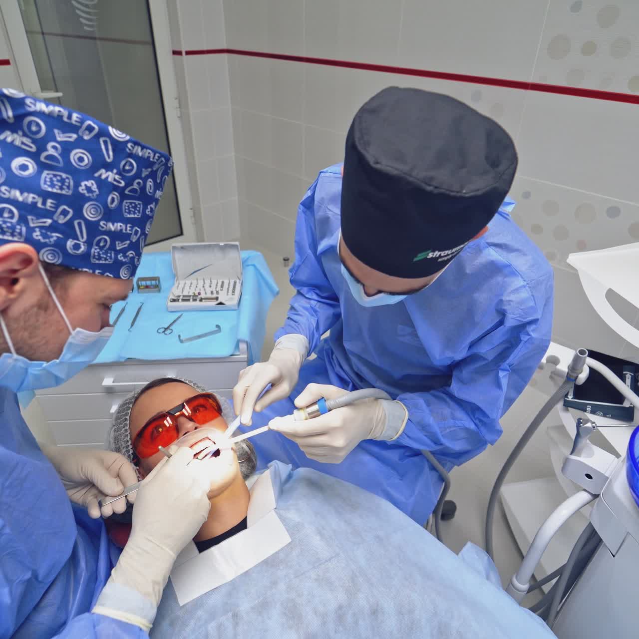 Dentist with assistant treating sick tooth to a patient. Woman patient in protective glasses lying in a dental chair. Top view.