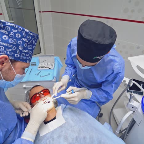 dentist with assistant treating sick tooth to a patient. woman patient in protective glasses lying in a dental chair. top view.