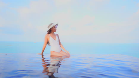 stunning asian model woman sitting at the edge of the infinity pool, front view