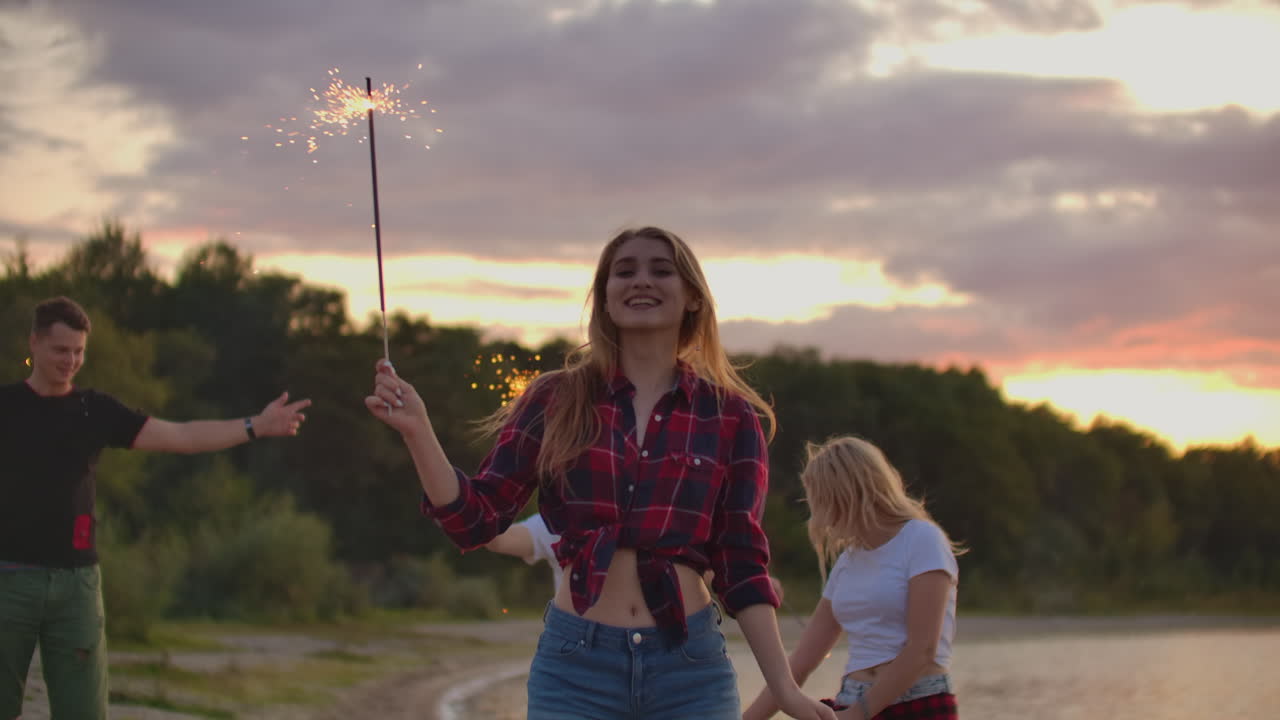 la joven está bailando con grandes luces de bengala en sus manos en la naturaleza con sus amigos. esta es una hermosa noche de verano en la fiesta al aire libre.