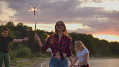 Das-Junge-Mädchen-Tanzt-Mit-Großen-Bengalischen-Lichtern-In-Ihren-Händen-Mit-Ihren-Freunden-In-Der-Natur.-Dies-Ist-Ein-Wunderschöner-Sommerabend-Auf-Einer-Open-Air-Party.