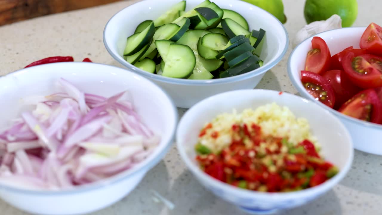 Bowls of sliced vegetables on a kitchen counter under bright lighting, showcasing preparation for a meal